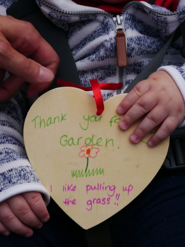 babu holding WOODEN hEART SAYING THANK YOU FOR TH GARDEN I LIKE PULLING UP GRASS.. WRITTEN ON IT